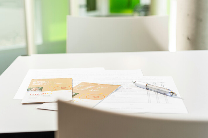 Tisch mit Formularen, Stift und Informationskarten für Patienten zum Download oder Ausfüllen.